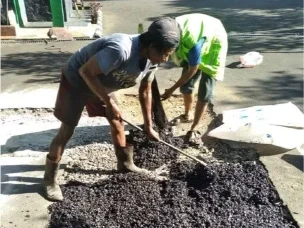 dua pekerja meratakan material aspal pada jalan